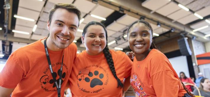 three smiling students in orange shirts